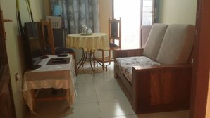 Una habitación con un sofá de madera, una mesita con mantel de encaje y una mesa de comedor con sillas.