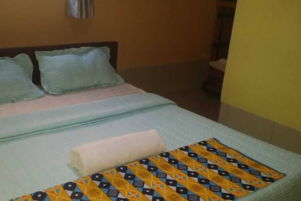 A bed with a patterned blanket, pillows, and a folded towel.