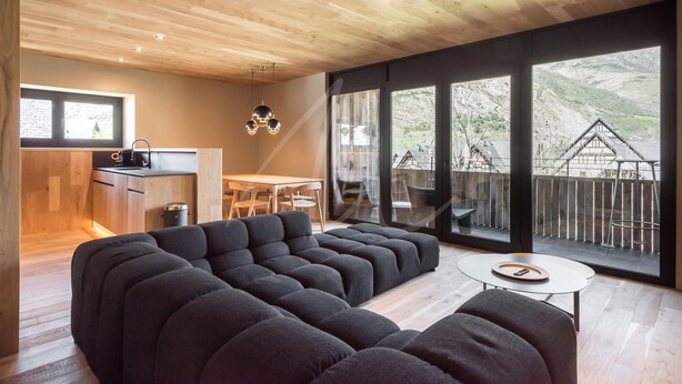 A modern living room with a sectional sofa, a small round table, and a view of a mountainous landscape through large windows. - Montardo (Artíes)