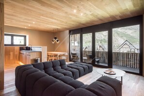 A modern living room with a sectional sofa, a small round table, and a view of a mountainous landscape through large windows. - Montardo (Artíes)