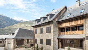 A stone building with wooden paneling and multiple windows, set against a mountainous backdrop. - Montardo (Artíes)