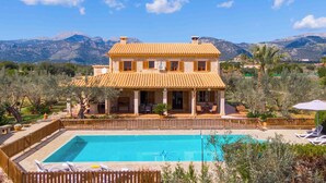 Una casa de dos pisos con piscina, rodeada de árboles y montañas.