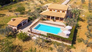 Una casa grande con piscina, rodeada de árboles y un patio cercado.