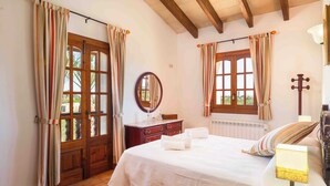 Un dormitorio con cama, cómoda, espejo, ventana con cortinas y lámpara.