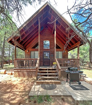 Une cabane en bois avec un porche, un barbecue et une petite terrasse.