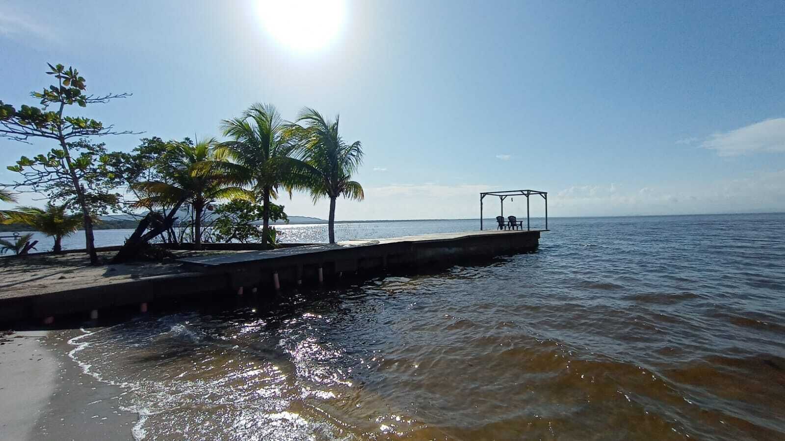 A pier extending into calm waters with palm trees and a gazebo.
