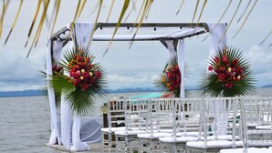 Une décoration de mariage comprenant une terrasse en bois, des chaises blanches et des arrangements floraux.