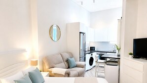Un dormitorio moderno con una cama grande, un sofá, un televisor y una kitchenette al fondo.