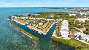 Luftaufnahme eines Küstenresorts mit mehreren Gebäuden, einer Marina und klarem, blauem Wasser.