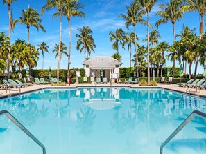 A pool with lounge chairs and palm trees, surrounded by a building with a grey roof.