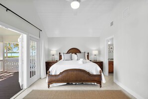 A bedroom with a wooden bed, white bedding, two bedside tables with lamps, and a view of the outdoors.
