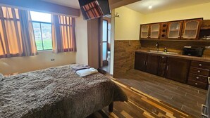 A bedroom with a large bed, a view of the outdoors through a window, and a kitchenette with wooden cabinets and a microwave. - beautiful and warm apartment,  5 minutes from Cusco airport (Cusco)