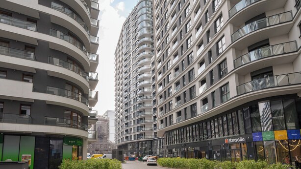 A modern high-rise building with multiple balconies, a storefront with a sign, and a clear sky. - Bright Crystal Premium Apartment (Warszawa)