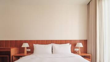 Habitación de hotel con una cama grande, cabecera de madera, dos mesitas de noche con lámparas y un ventanal con cortinas.