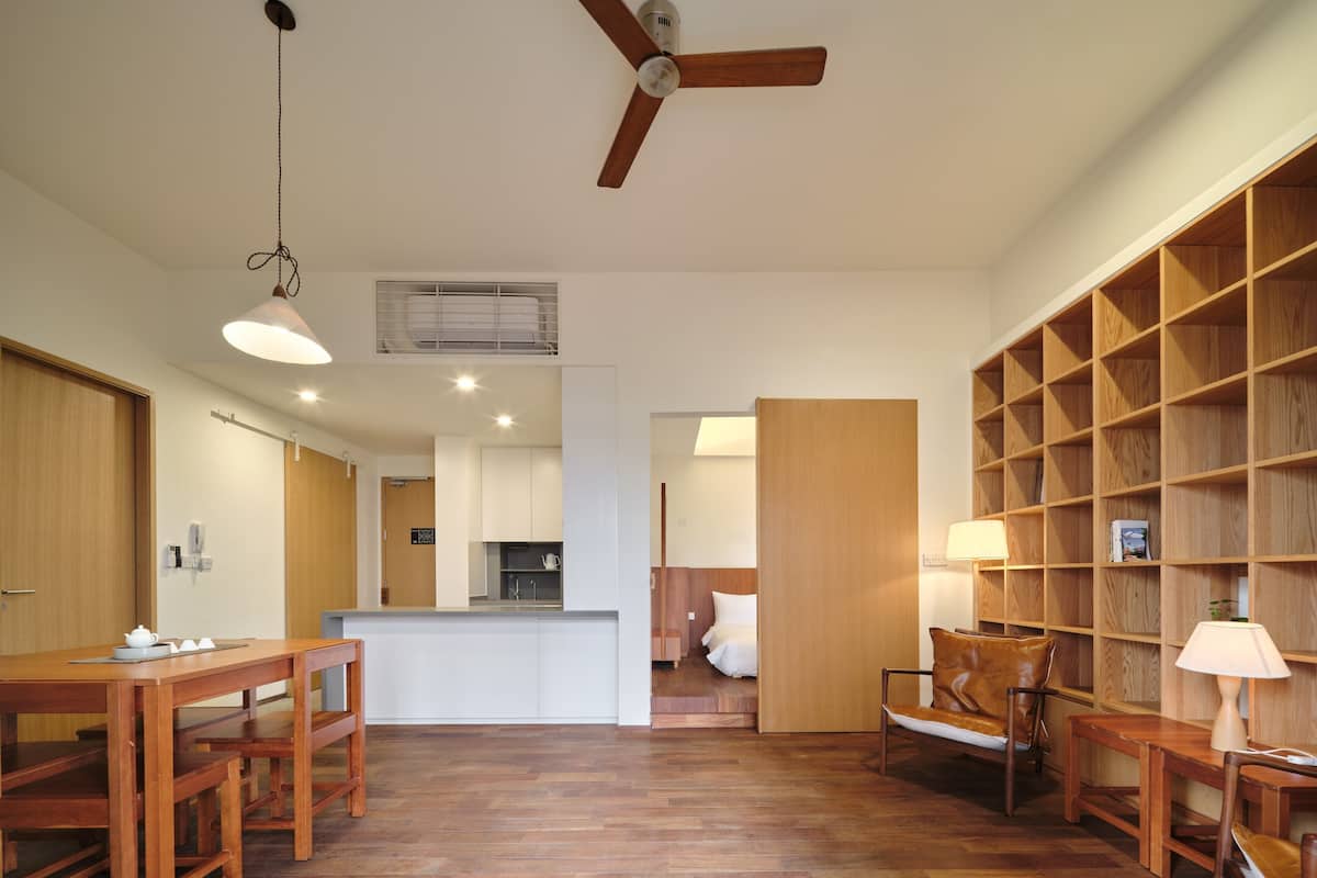 Ein geräumiger Wohnbereich mit Holzboden, Deckenventilator, Esstisch mit Stühlen, Bücherregal und einer Küche im Hintergrund.