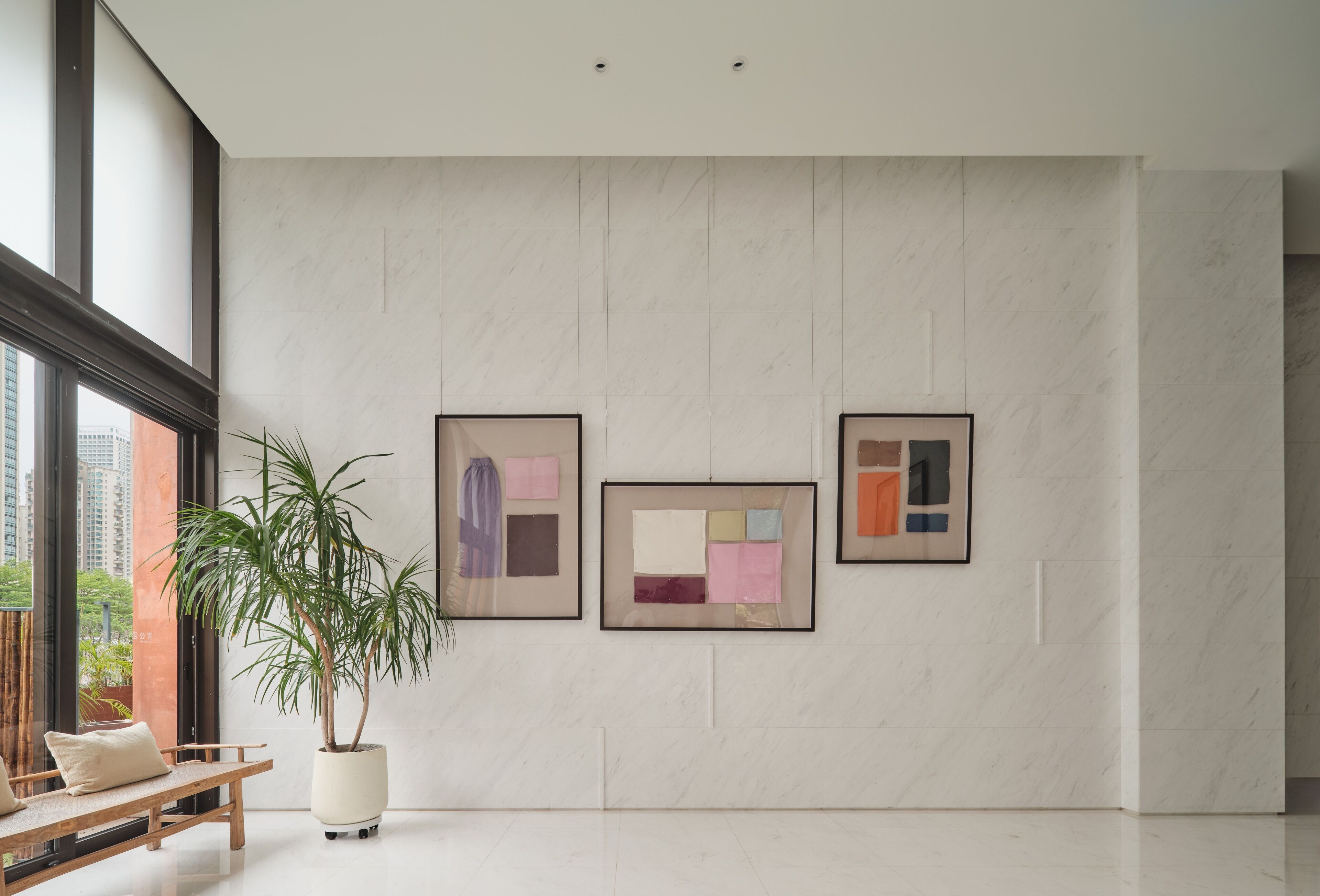 A modern interior with a large window, a potted plant, and three framed artworks on the wall.