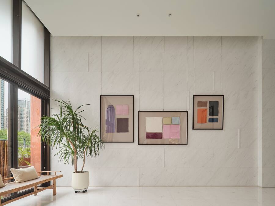 A modern interior with a large window, a potted plant, and three framed artworks on the wall.