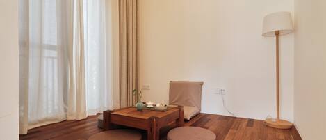 A modern room with a wooden floor, a round table with a cushion, a lamp, and a chair.