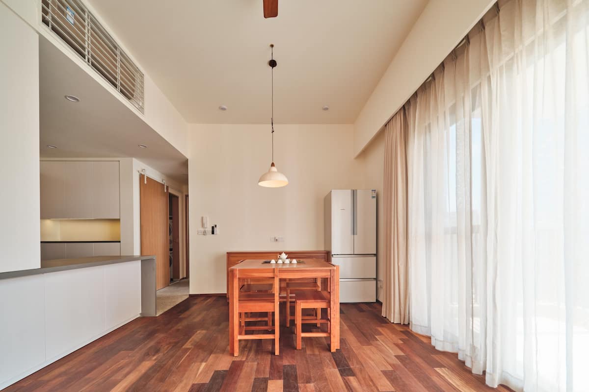 Eine moderne Küche mit Holzboden, einem Esstisch mit Stühlen, einer Pendelleuchte und einem Kühlschrank.