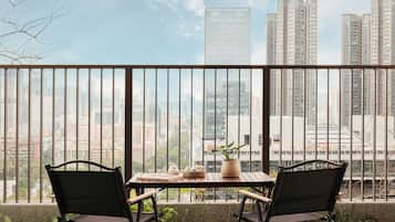 A balcony with two black chairs and a wooden table, overlooking a cityscape with tall buildings.