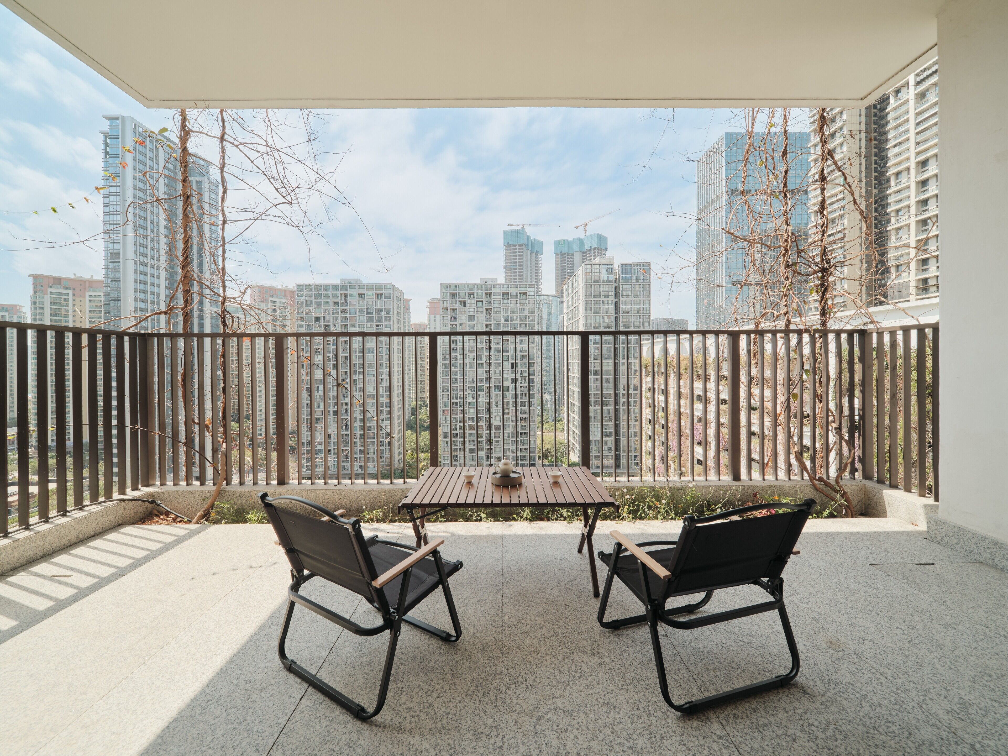 A balcony with two chairs and a table, overlooking a cityscape with high-rise buildings.