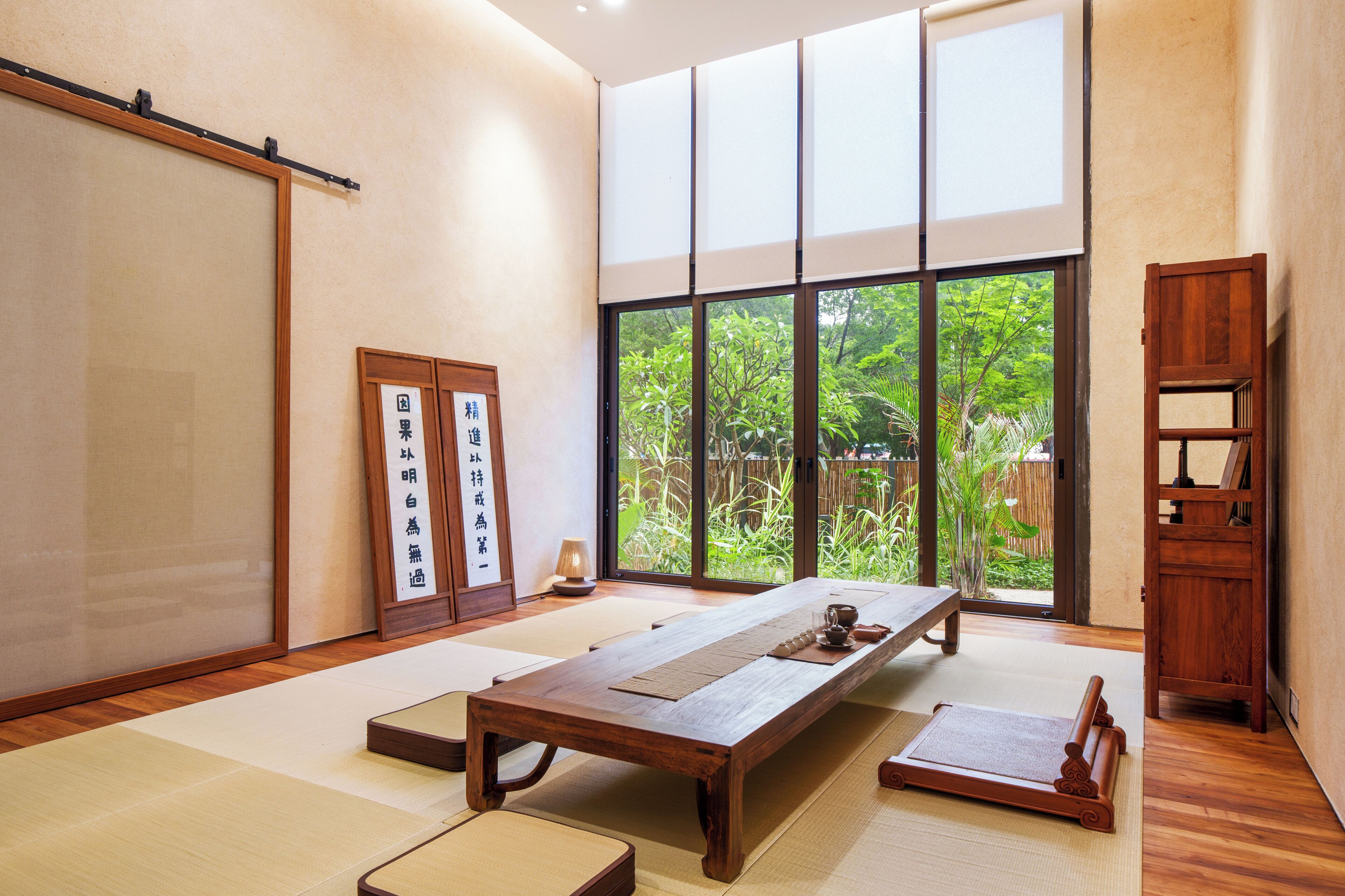 Una habitación japonesa tradicional con suelo de tatami, una mesa de madera baja, puertas correderas y vistas a la vegetación exterior.