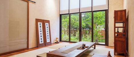 Una habitación japonesa tradicional con suelo de tatami, una mesa de madera baja, puertas correderas y vistas a la vegetación exterior.