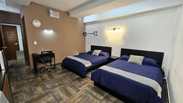 A hotel room with two beds, a desk, a chair, a clock, and a wall-mounted light fixture.