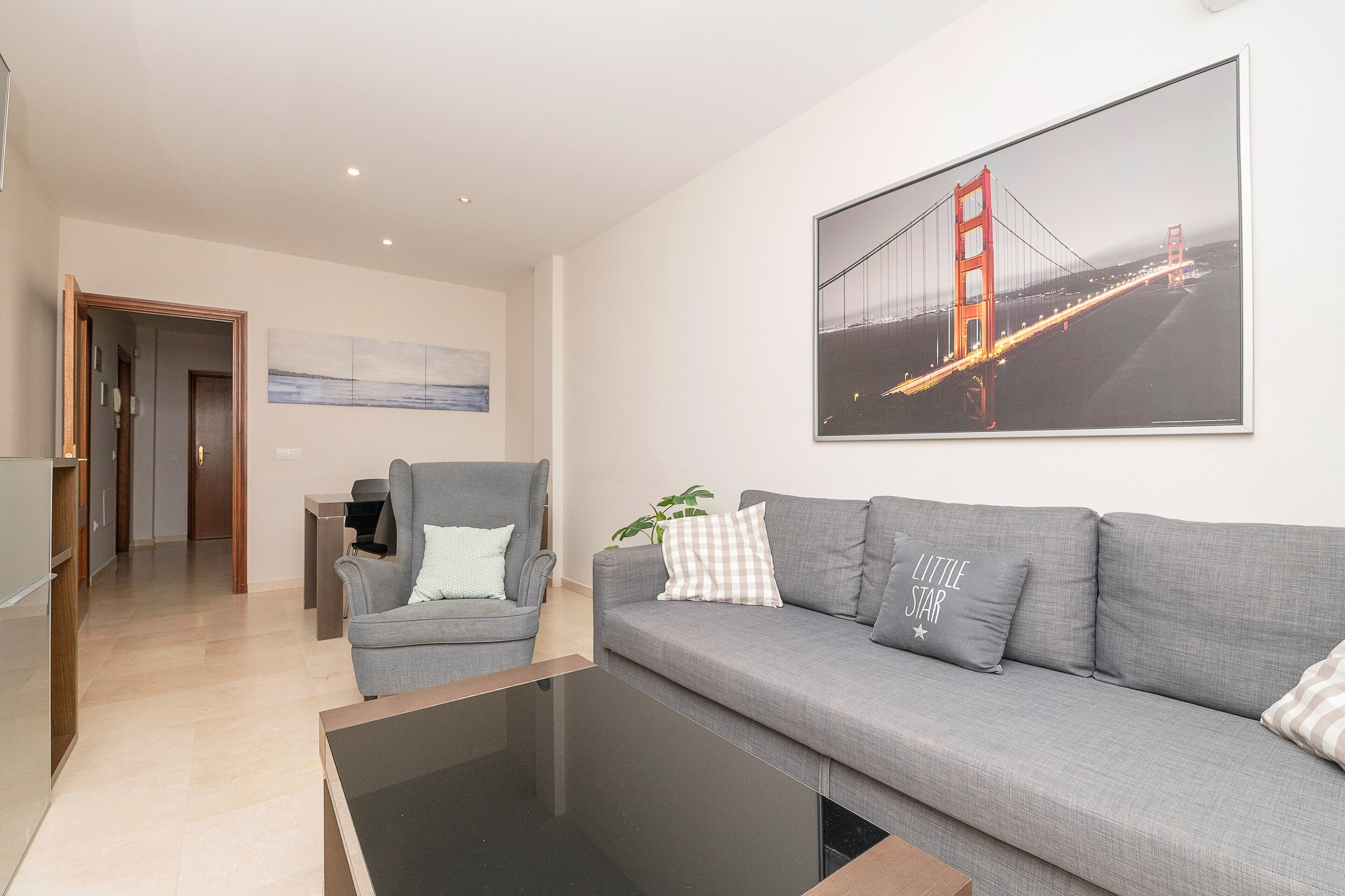 Een moderne woonkamer met een grijze bank, een grijze fauteuil en een salontafel. Op de muur hangt een groot fotokader van de Golden Gate Bridge.
