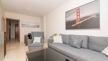 Een moderne woonkamer met een grijze bank, een grijze fauteuil en een salontafel. Op de muur hangt een groot fotokader van de Golden Gate Bridge.