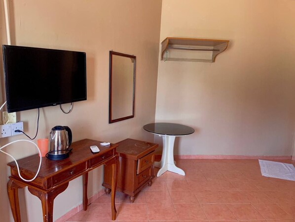 A room with a wooden desk, a small table, a television mounted on the wall, a mirror, and a shelf.