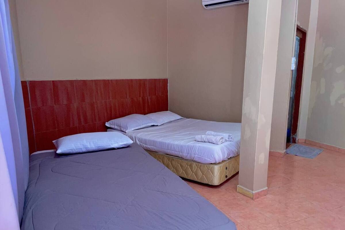 A room with two beds, one with a red headboard and one with a beige headboard, both with white bedding.