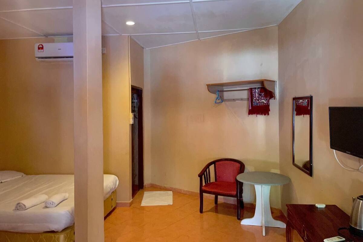 A room with a bed, a chair, a small table, a TV, and a shelf with a mirror.