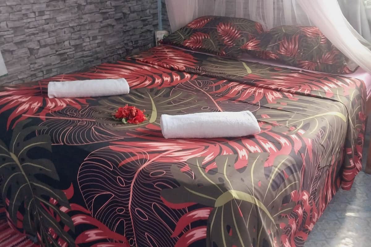 Ein Bett mit einem blumigen Überwurf, einem weißen Handtuch und einer roten Blume darauf.