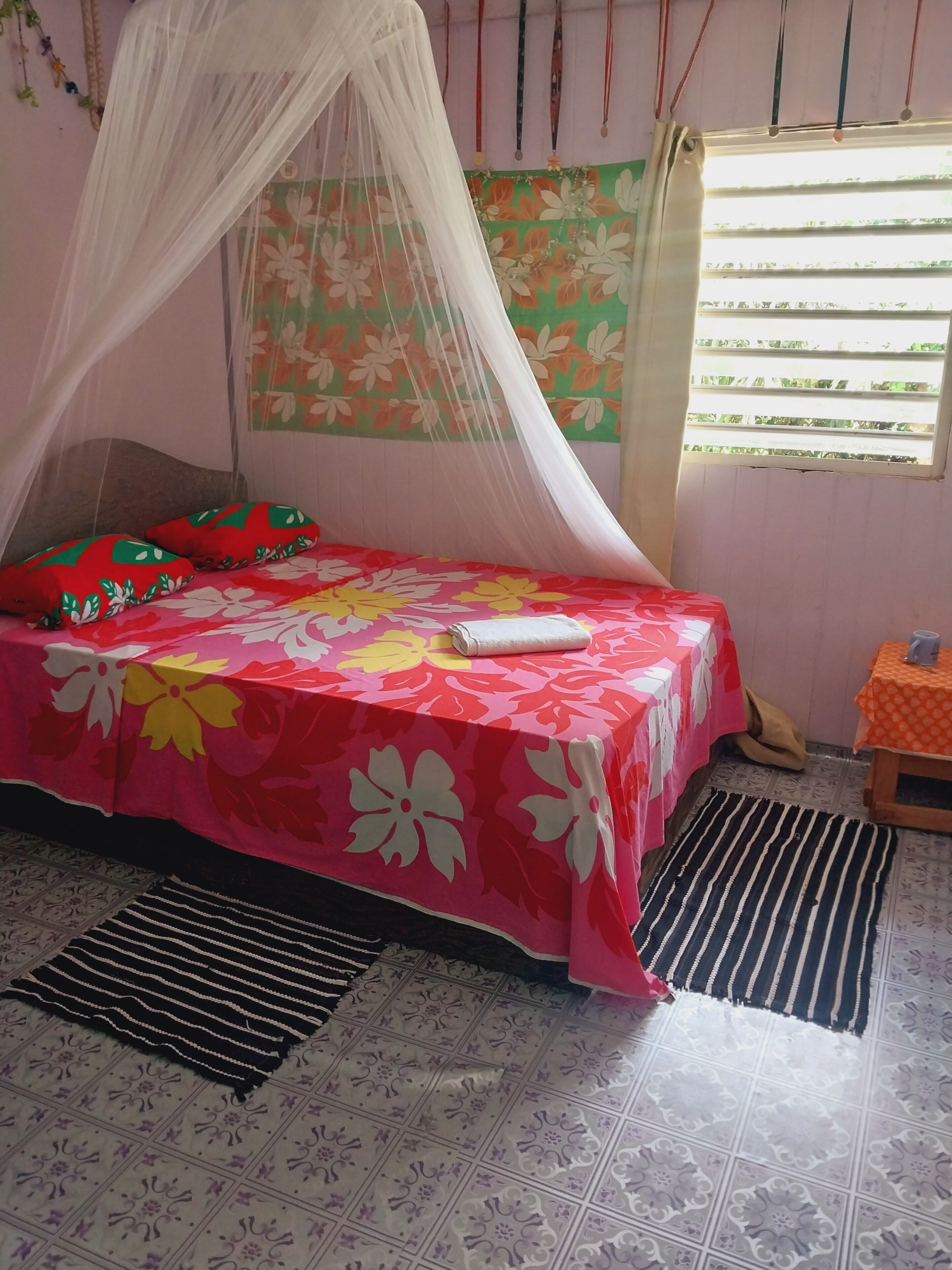 Una habitación con una cama cubierta por una colcha floral, una mosquitera y una ventana con persianas.
