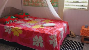 Una habitación con una cama cubierta por una colcha floral, una mosquitera y una ventana con persianas.