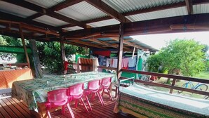 An outdoor covered dining area with a wooden deck, a table with a tablecloth, and several plastic chairs. - Tapuhere Lodge (Huahine)
