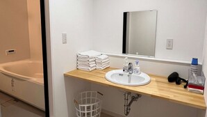 Ein Badezimmer mit einer Badewanne, einem Waschbecken mit Handseife, einem Spiegel und einem Stapel Handtücher.