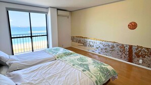 Ein Zimmer mit zwei Betten, einem großen Fenster mit Meerblick und einer Wand mit abblätternder Farbe.