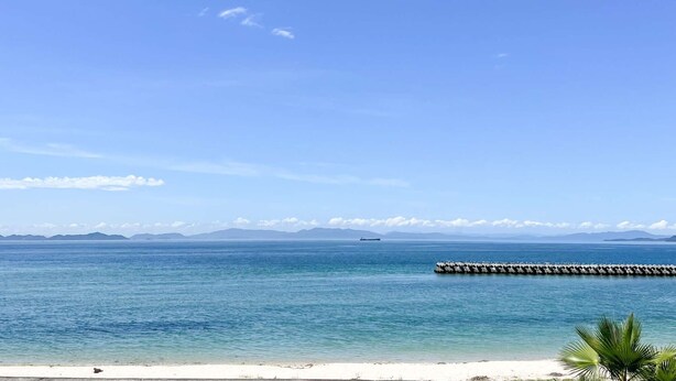 Ein Strand mit klarem, blauem Wasser, weißem Sand und einer langen Pier, die sich ins Meer erstreckt.
