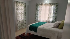 Un dormitorio con cama, una manta verde y cortinas con estampado de hojas.