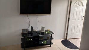 Una habitación con un televisor montado, un mueble negro para entretenimiento con dispositivos electrónicos, y una puerta con diseño decorativo.