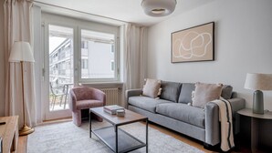 Un salon moderne avec un canapé gris, un fauteuil rose, une table basse et une table d’appoint avec une lampe.