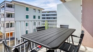 Un balcon avec une table et des chaises, donnant sur un immeuble doté de nombreux balcons et fenêtres.