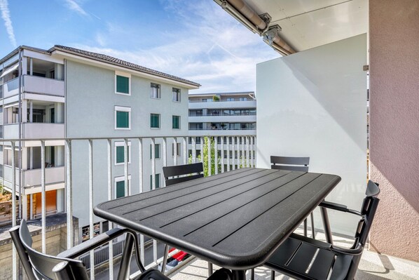 A balcony with a table and chairs, overlooking a building with multiple balconies and windows.