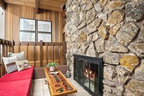 Una habitación acogedora con pared de piedra, chimenea, banca de madera, sofá rojo y mapas enmarcados en la pared.