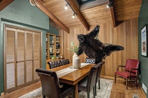 Un comedor con una mesa de madera, sillas de cuero, una estatua de oso y techo de madera.