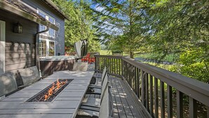 Una terraza con una chimenea, mobiliario exterior y vistas a un área boscosa.
