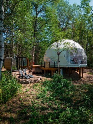 A dome-shaped eco-lodge surrounded by trees, with a wooden deck and outdoor seating area. - Refuge Bay Aer XL Dome - Luxury Off Grid Escape (Cherhill)