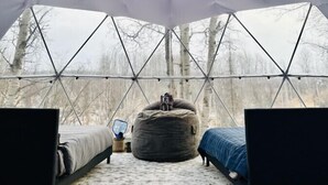Una carpa con estructura de techo geométrica, dos camas y un sillón de tina.